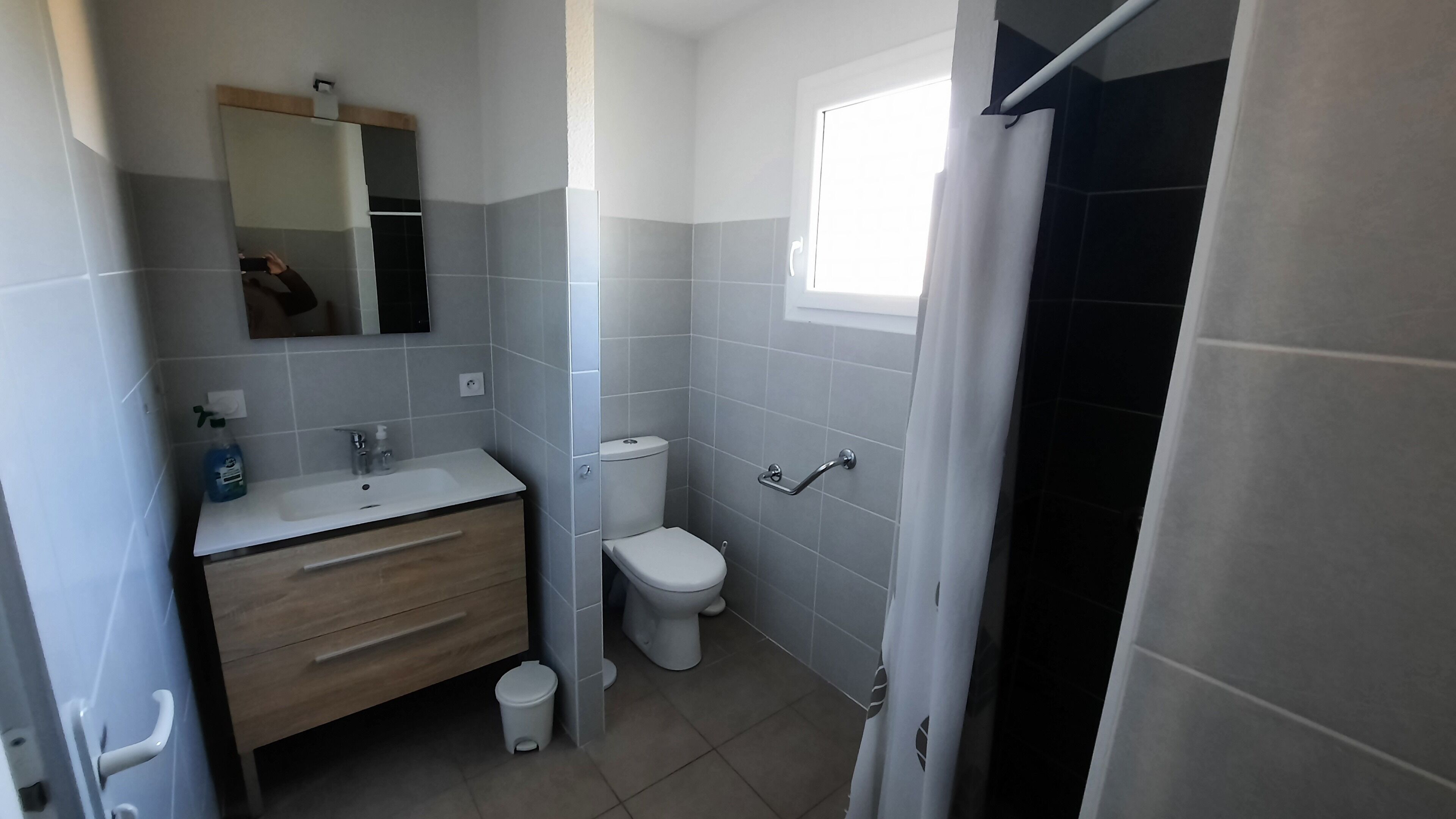 Ein Badezimmer mit weißem Waschbecken, Spiegel und Toilette, mit grauen und schwarzen Fliesen.