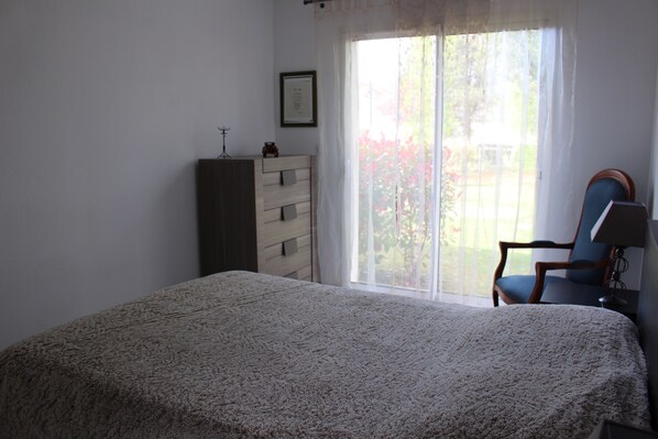 A bedroom with a bed, a dresser, a chair, and a window with curtains. - Bungalow, large lot, near a lake and the ocean (Hourtin)