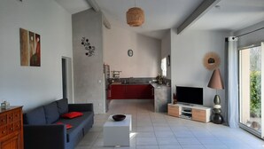 A modern living room with a sofa, coffee table, TV, and a kitchen in the background. - Single-storey villa, large plot, close to lake and ocean (Hourtin)