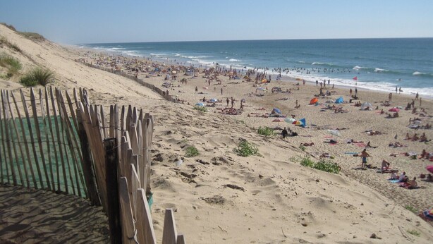 A beach with a wooden fence and a sandy area with umbrellas and people. - Single-storey villa, large plot, close to lake and ocean (Hourtin)