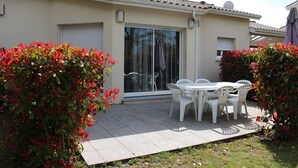 A patio area with a table and chairs, surrounded by greenery and a building with a tiled roof. - Single-storey villa, large plot, close to lake and ocean (Hourtin)