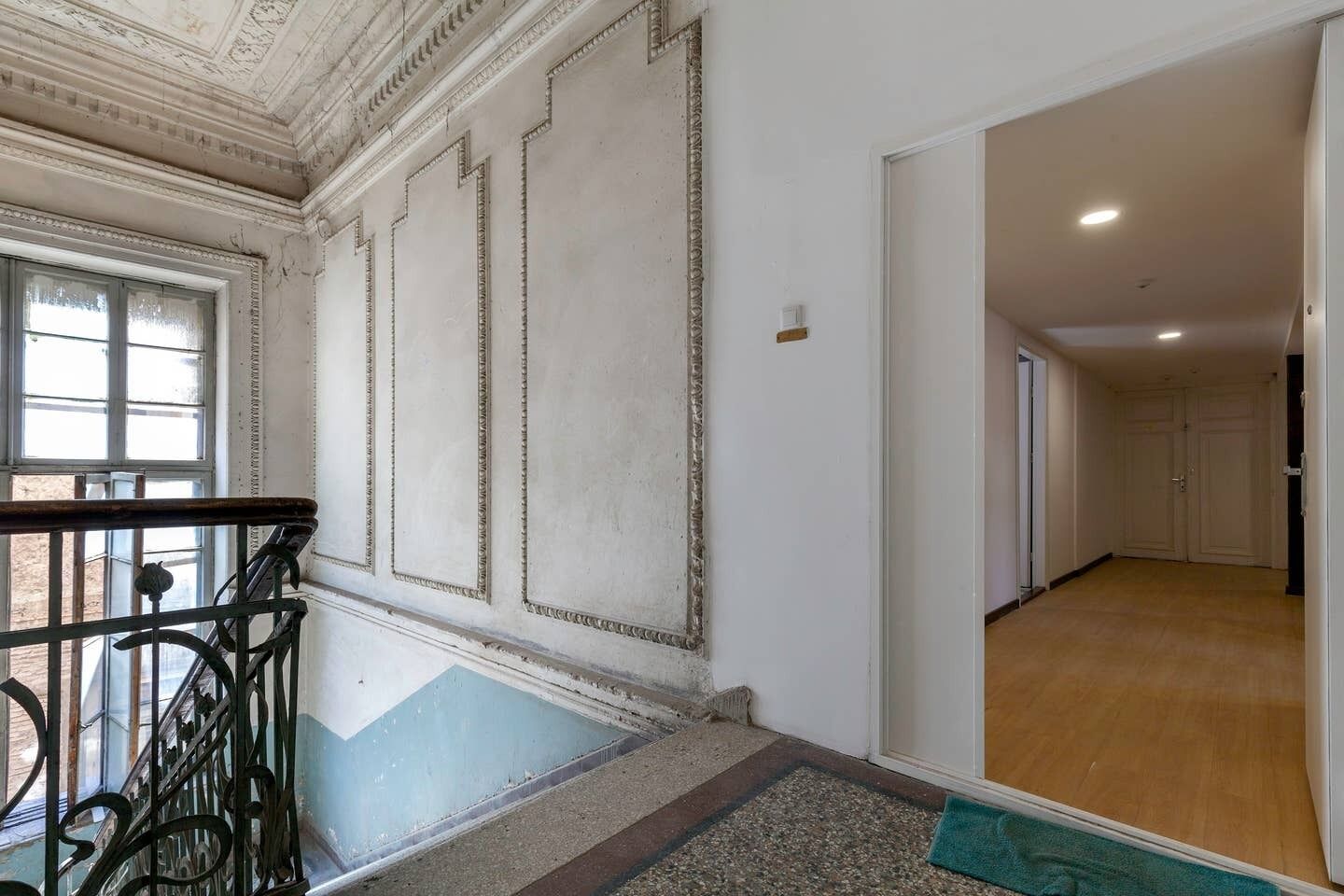 Un passadís amb terra de fusta, una escala amb barana metàl·lica i una porta que dona a una altra habitació.
