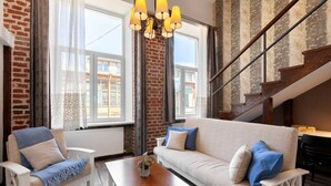A modern living room with a sofa, armchairs, and a coffee table. There is a staircase with a wooden railing and a view of the outside through large windows. - Cozy Studios on Freedom Square (Tbilisi)