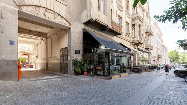 A cobblestone street with a building featuring a glass storefront and a black awning. - Cozy Studios on Freedom Square (Tbilisi)