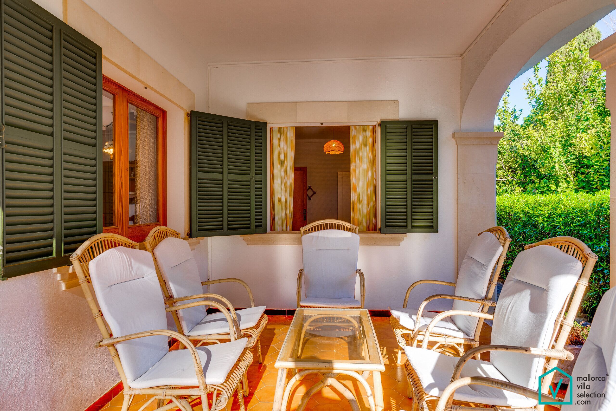 A covered patio with wicker furniture and a glass table.