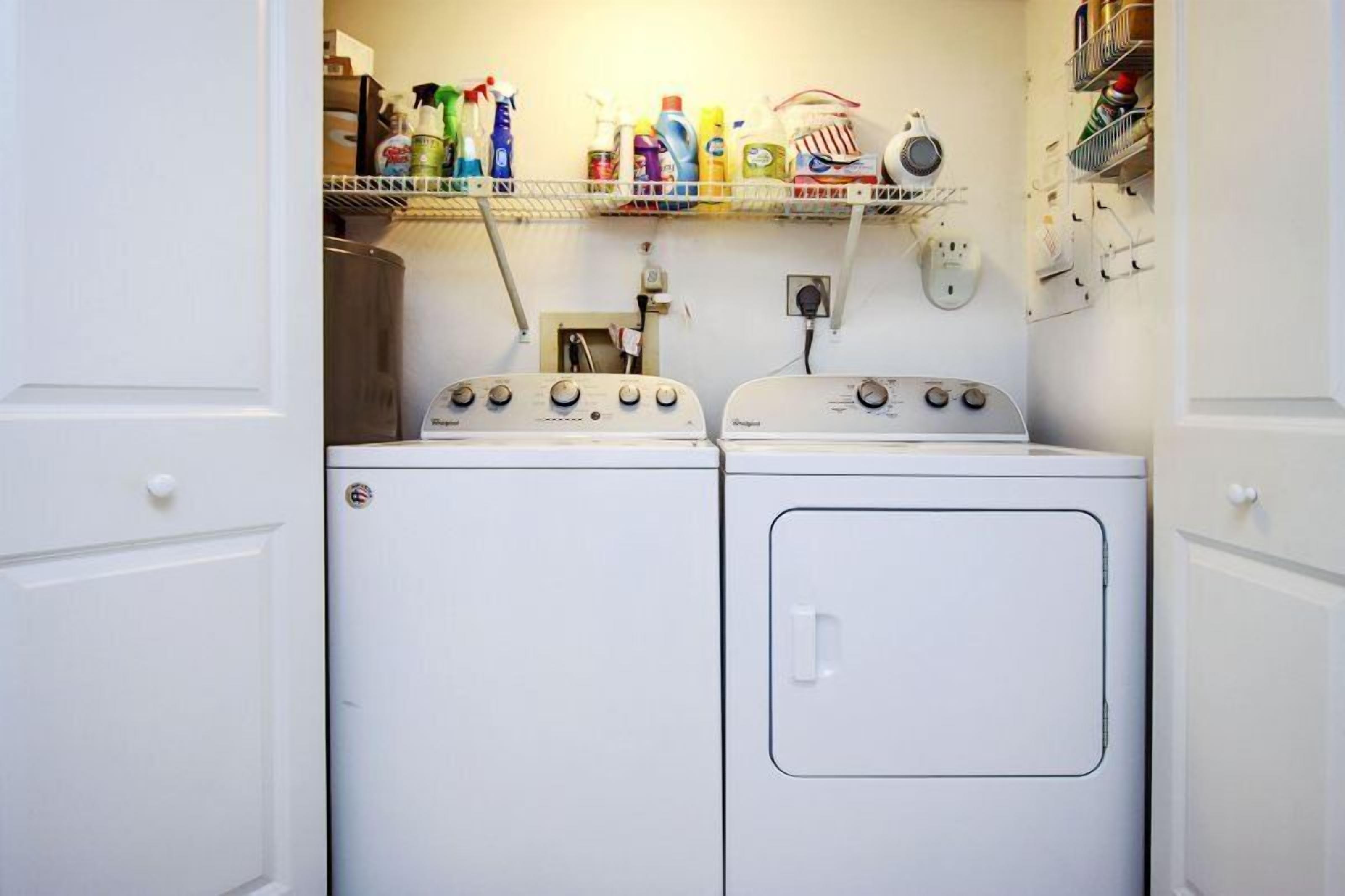 A laundry area with two washing machines, a shelf with cleaning supplies, and a power outlet.