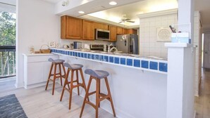 Uma cozinha com armários de madeira, micro-ondas, geladeira e uma ilha azulejada com banquetas.