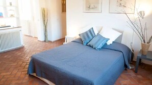 A bedroom with a large bed, white walls, and a radiator. There are two framed pictures on the wall and a small table with a lamp. - Spanish steps luxury loft apartment (Roma)