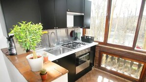 A compact kitchen with black cabinets, a stainless steel sink, and a built-in oven. There is a window providing natural light and a view of trees outside. - Spanish steps luxury loft apartment (Roma)