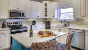 Een moderne keuken met witte kasten, roestvrijstalen apparatuur, een centraal eiland met een schoolbord en uitzicht op de omgeving.