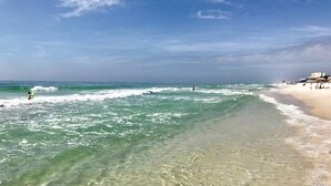 Een strand met helder ondiep water, een zandstrand en enkele mensen in de verte.