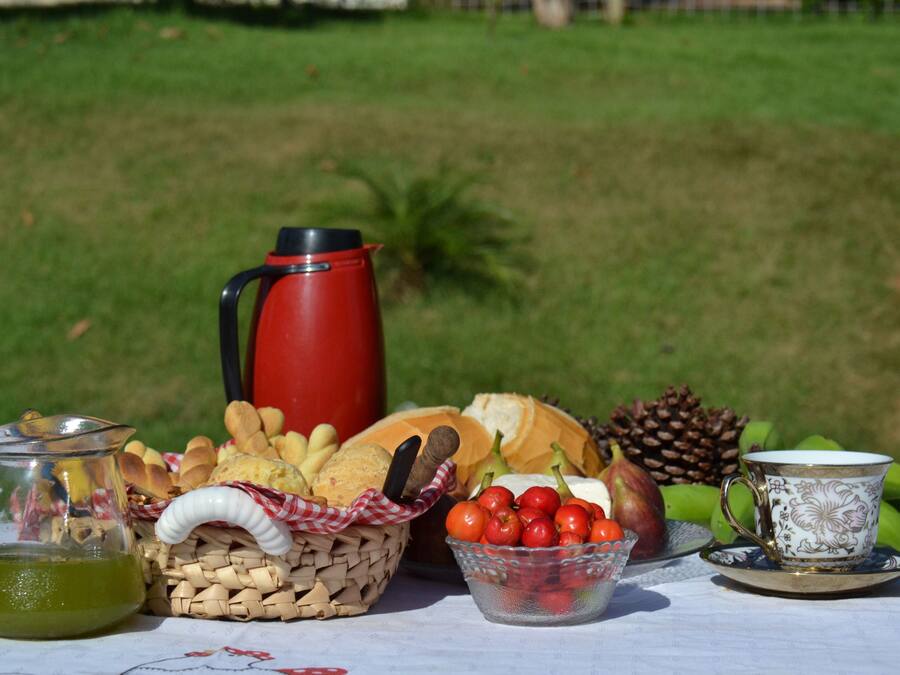 A picnic setup with a red coffee pot, bread, cheese, tomatoes, and a decorative cup on a table.