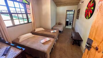 Habitació amb dos llits individuals, una panxa de fusta, escriptori amb un ordinador i finestra amb vista a vegetació.
