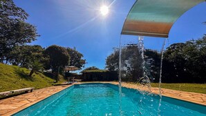 A swimming pool with clear blue water, surrounded by a stone deck and lush greenery. - Pousada Vale das Primaveras (Tres Coracoes)