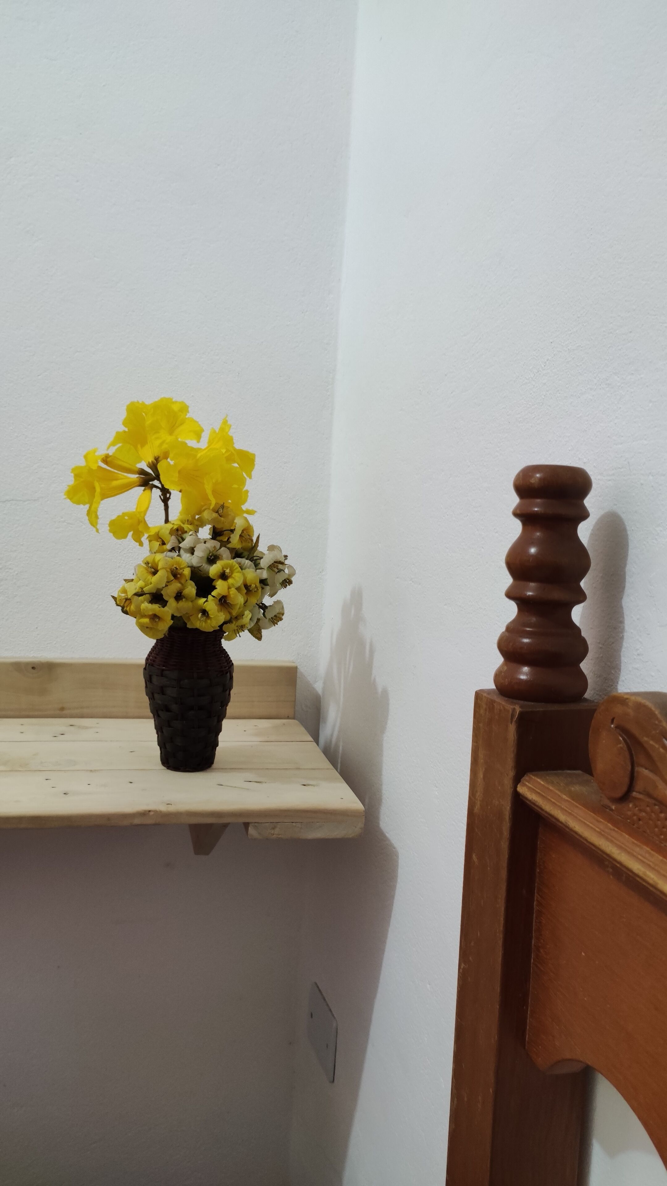 Una estantería de madera con un jarrón de flores amarillas frente a una pared blanca.