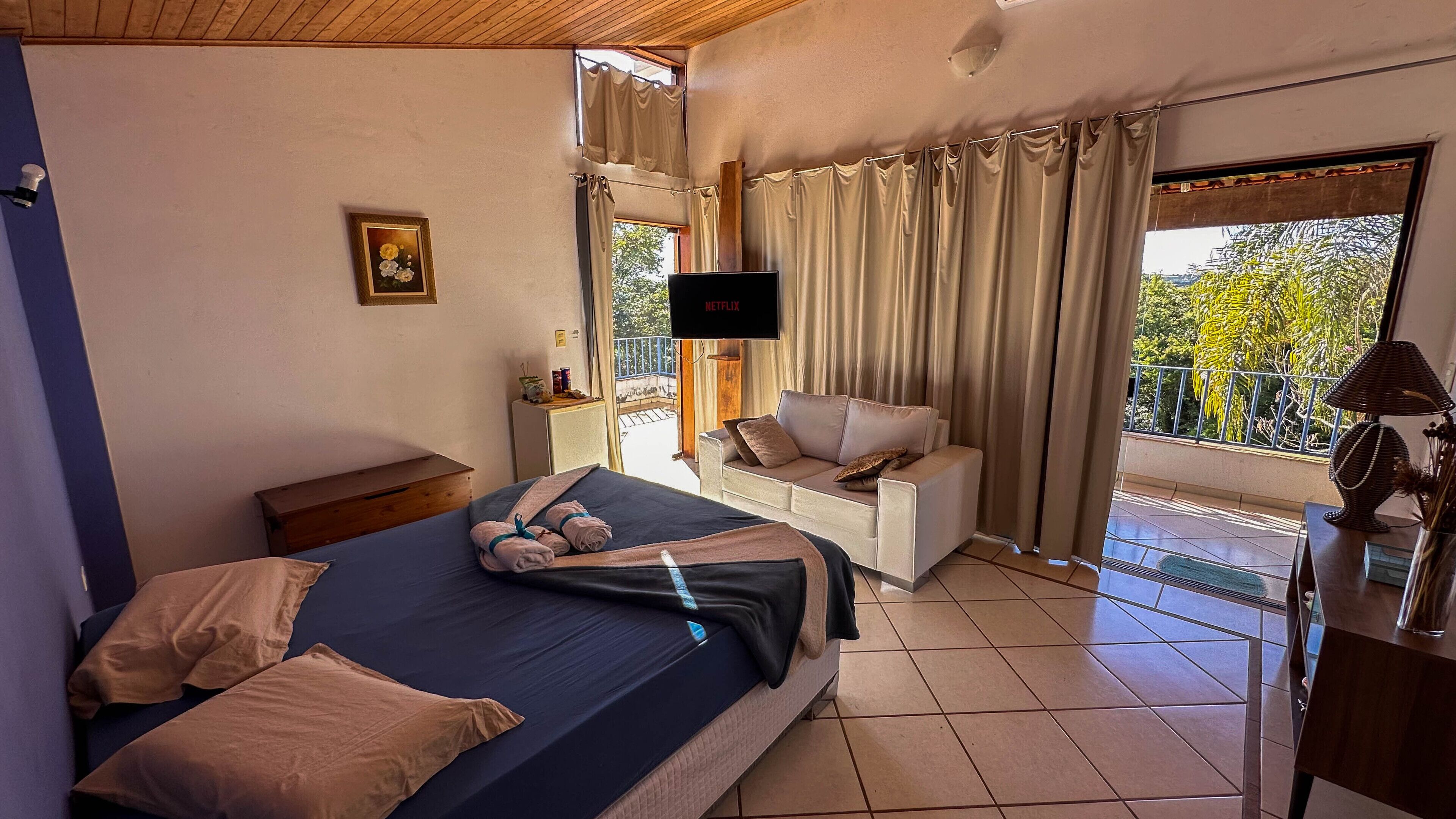 Une chambre à coucher avec un lit, un canapé, une télévision et une fenêtre avec des rideaux.