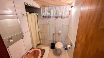 A small bathroom with a wooden bathtub, a toilet, and a sink.