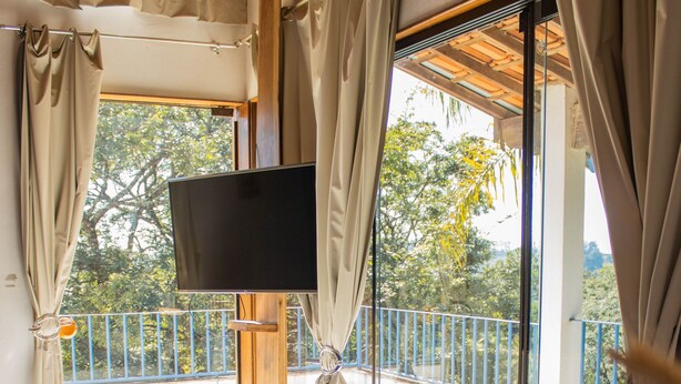 A living room with a sofa, a flat-screen TV, and a balcony with a railing. - Pousada Vale das Primaveras (Tres Coracoes)