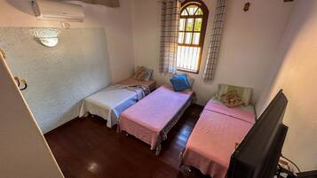 Quarto pequeno e acolhedor com duas camas de solteiro, uma janela com cortinas, piso de madeira e televisão.