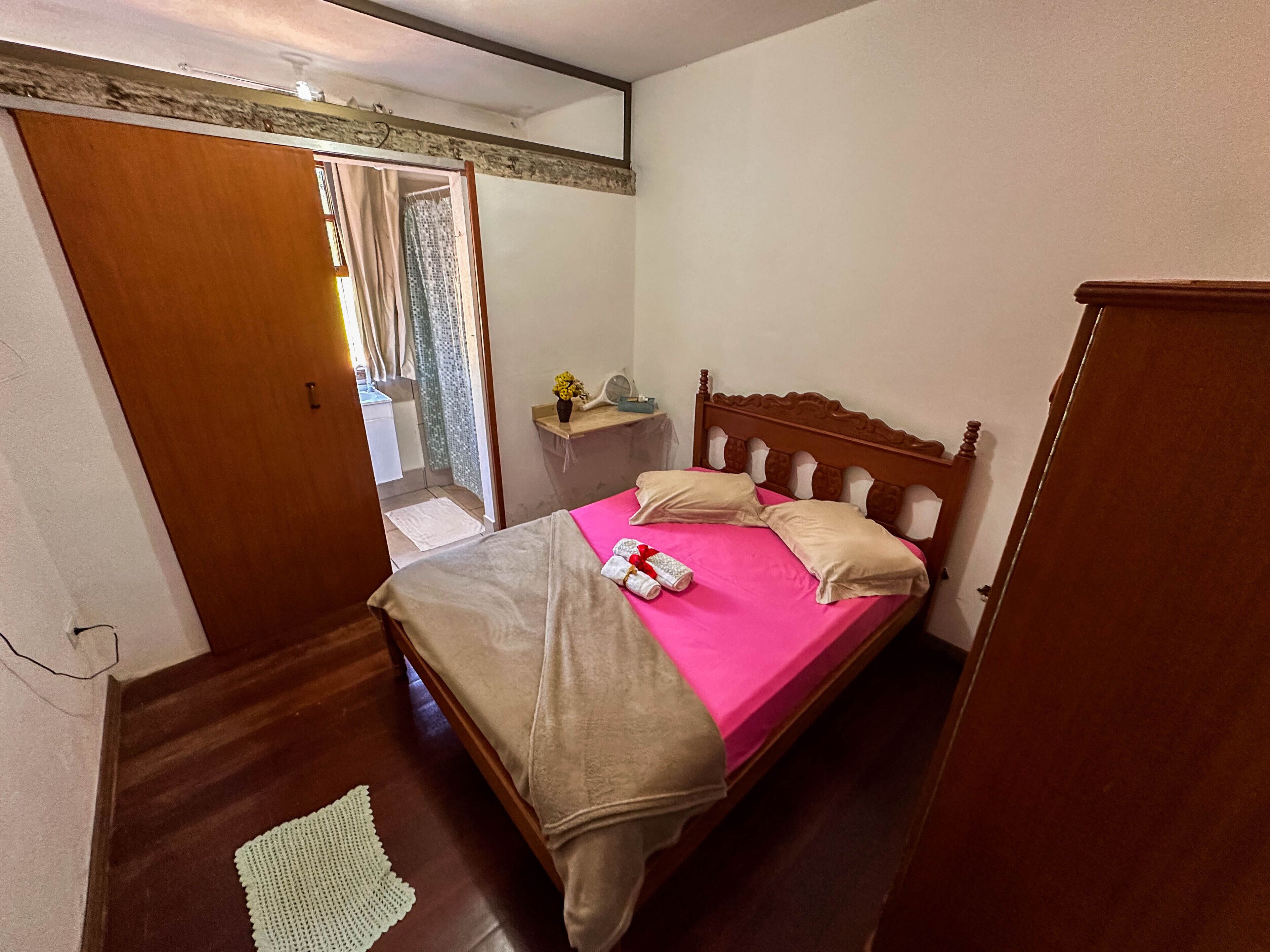A bedroom with a wooden bed, a small bedside table, a mirror, and a door leading to a balcony.