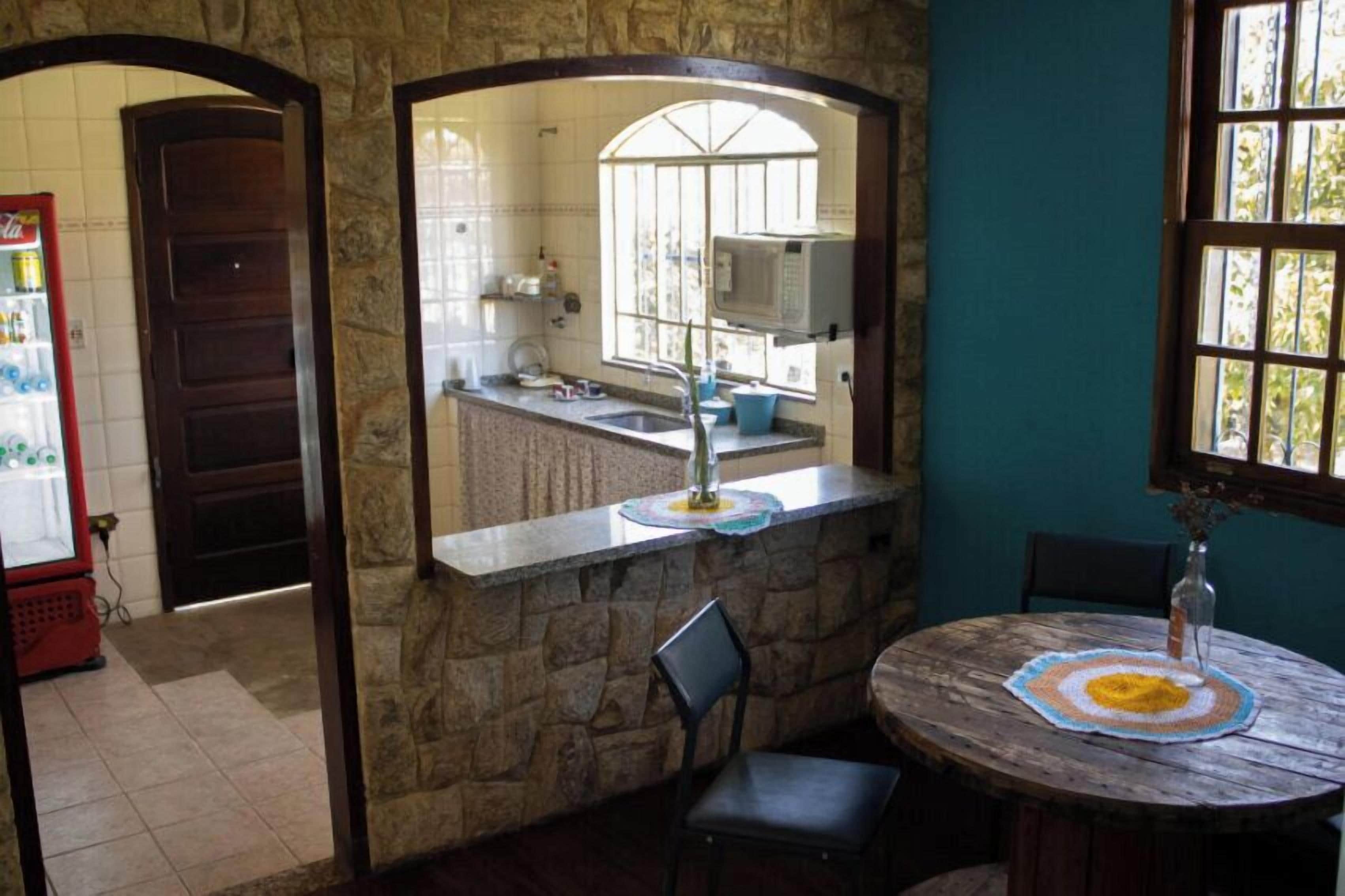 A kitchen with a stone counter, a sink, and a window. There is a microwave above the counter and a refrigerator in the background.