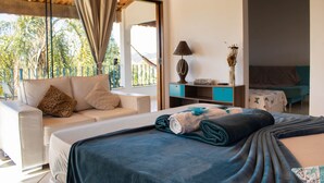 A hotel room with a bed, a sofa, a desk, and a view of palm trees. - Pousada Vale das Primaveras (Tres Coracoes)
