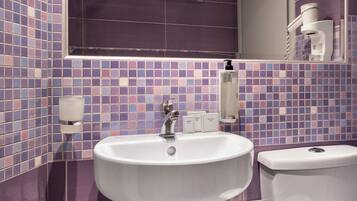 A bathroom with a white sink, a mirror, and a toilet. The walls are tiled with purple and blue tiles.