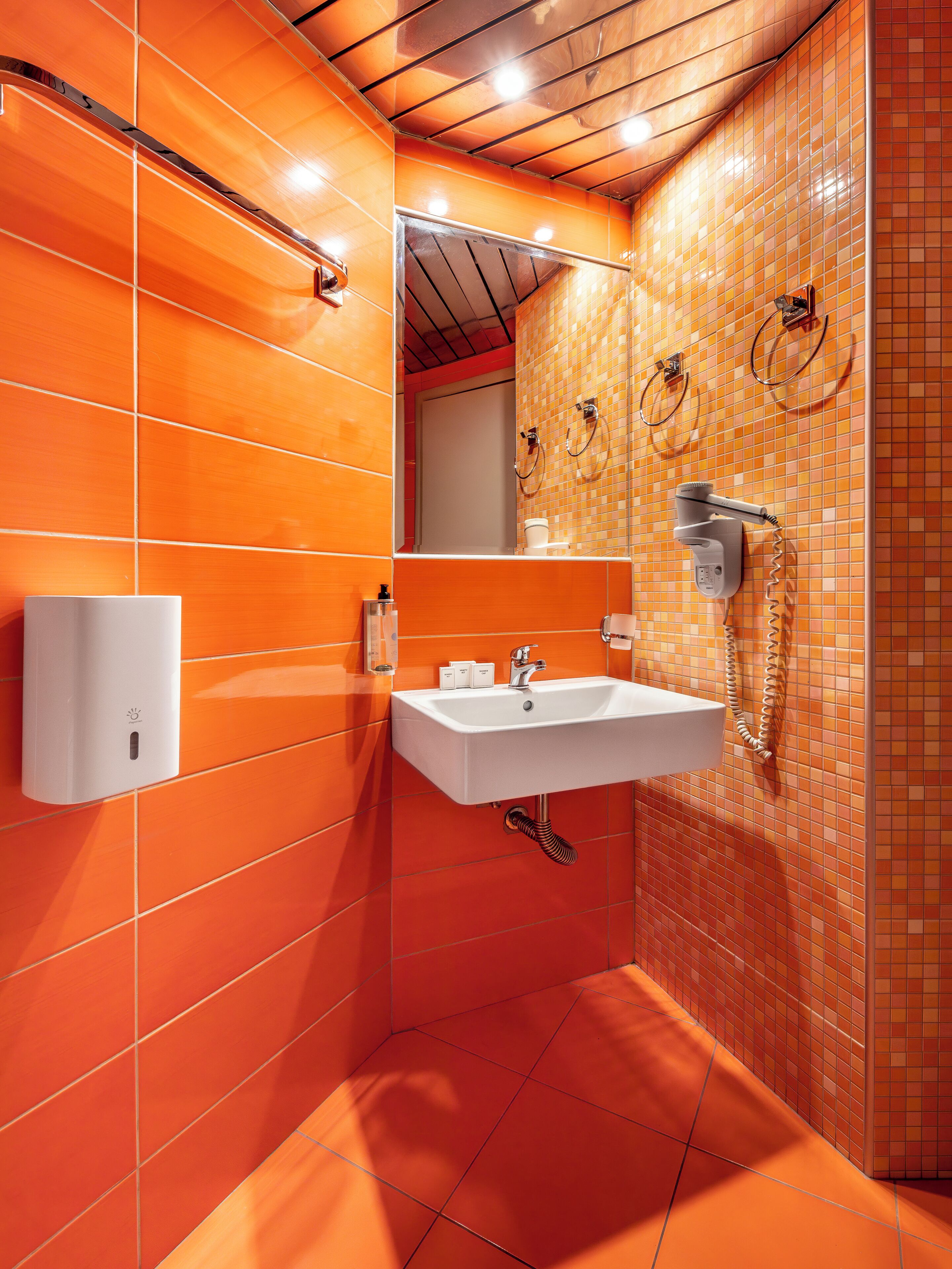 A bathroom with orange tiles, a white sink, a mirror, and a towel rack.