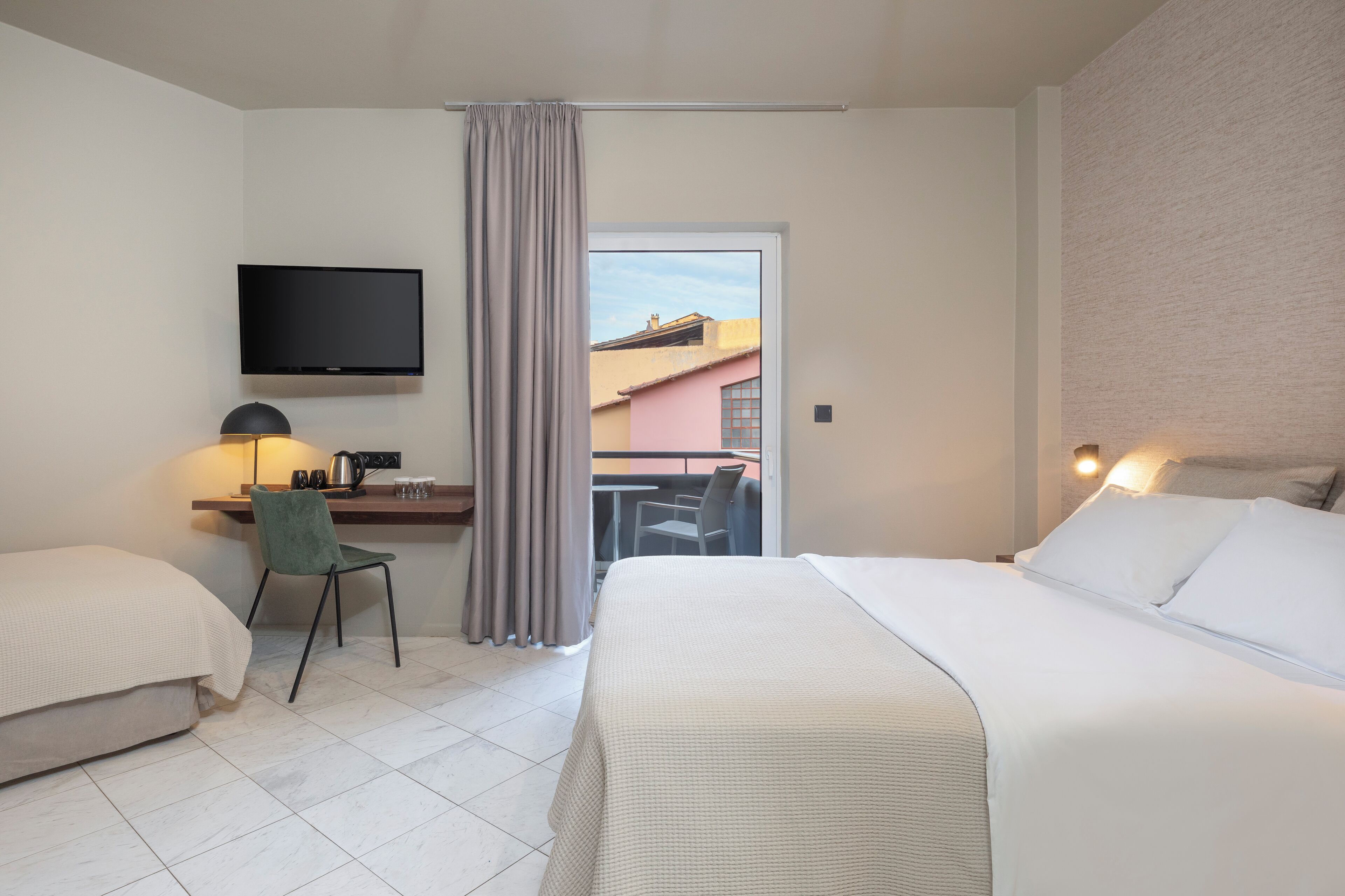 Habitación de hotel con una cama, un escritorio con silla, televisión y vistas a edificios.