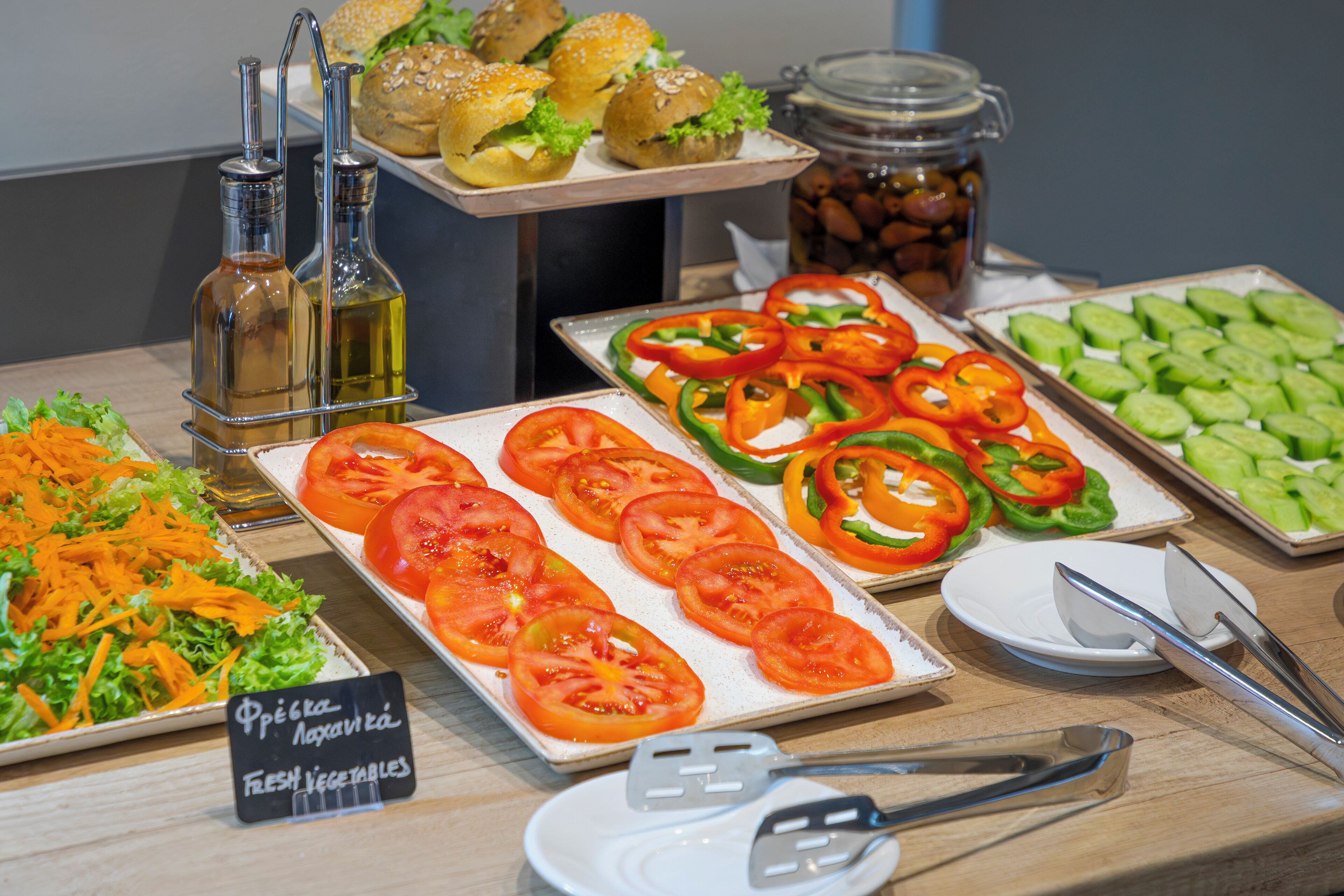 A buffet table with fresh vegetables, sandwiches, and condiments.