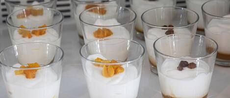 Une série de verres transparents contenant des desserts à plusieurs couches, avec une base au caramel, surmontés de crème fouettée et de morceaux de fruits.