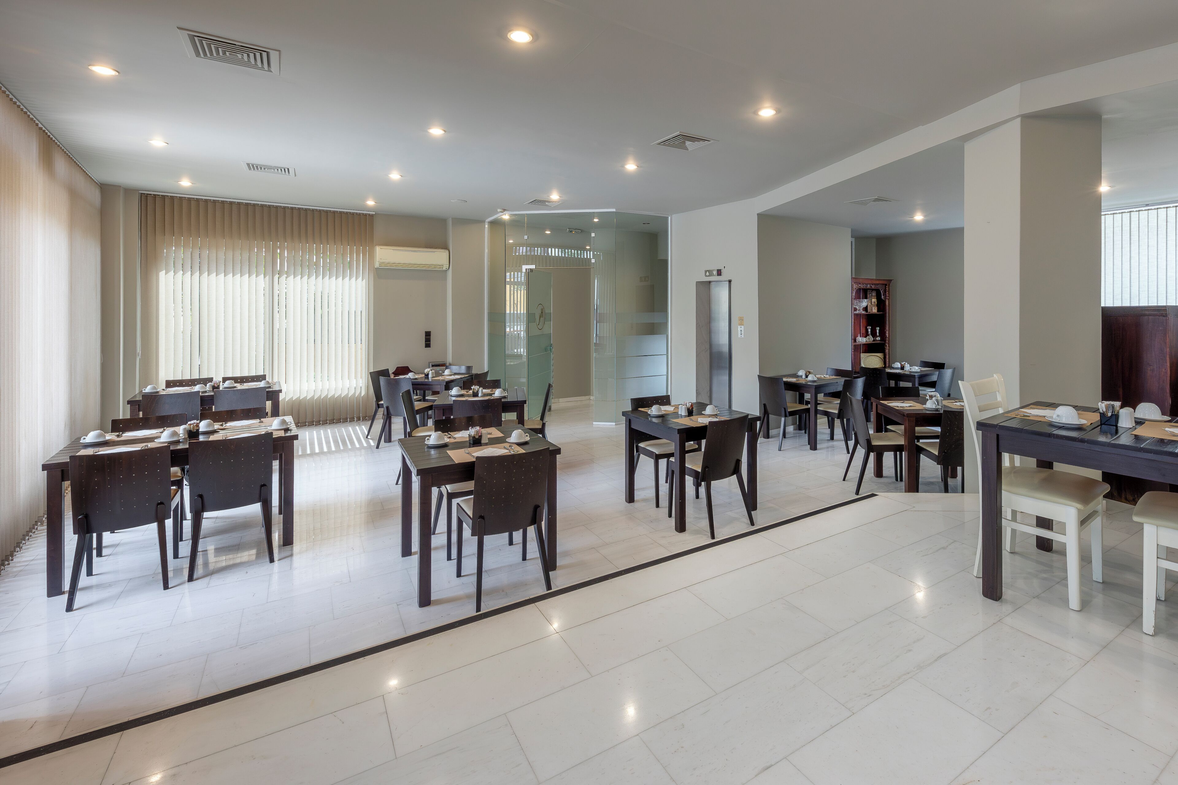 A spacious hotel dining area with multiple tables and chairs, a glass partition, and a modern interior design.