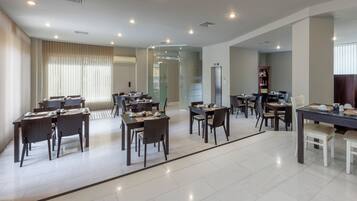 A spacious hotel dining area with multiple tables and chairs, a glass partition, and a modern interior design.