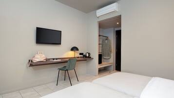 Ein Hotelzimmer mit einem Bett, einem Schreibtisch mit Stuhl, einem Fernseher, einem Kleiderständer und einer Klimaanlage.