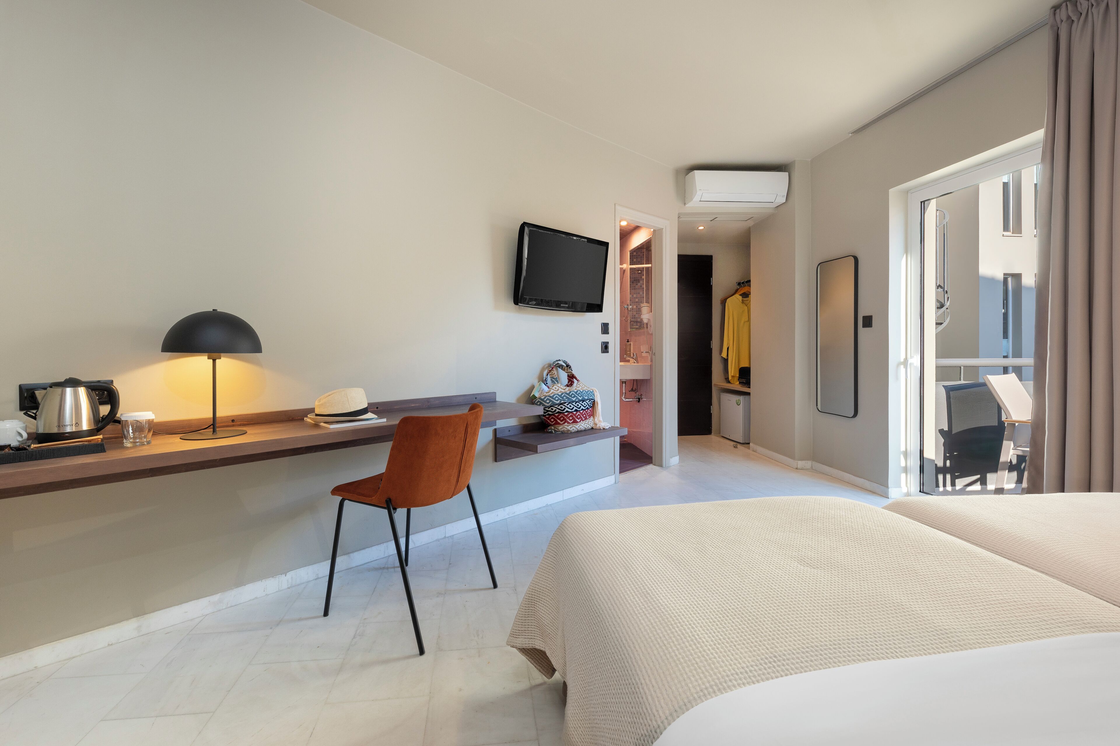 A hotel room with a bed, a desk with a chair, a television, and a bathroom visible through an open door.