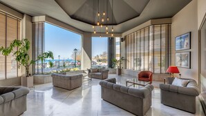 A spacious lounge area with multiple sofas and armchairs, large windows with blinds, and a hanging light fixture.