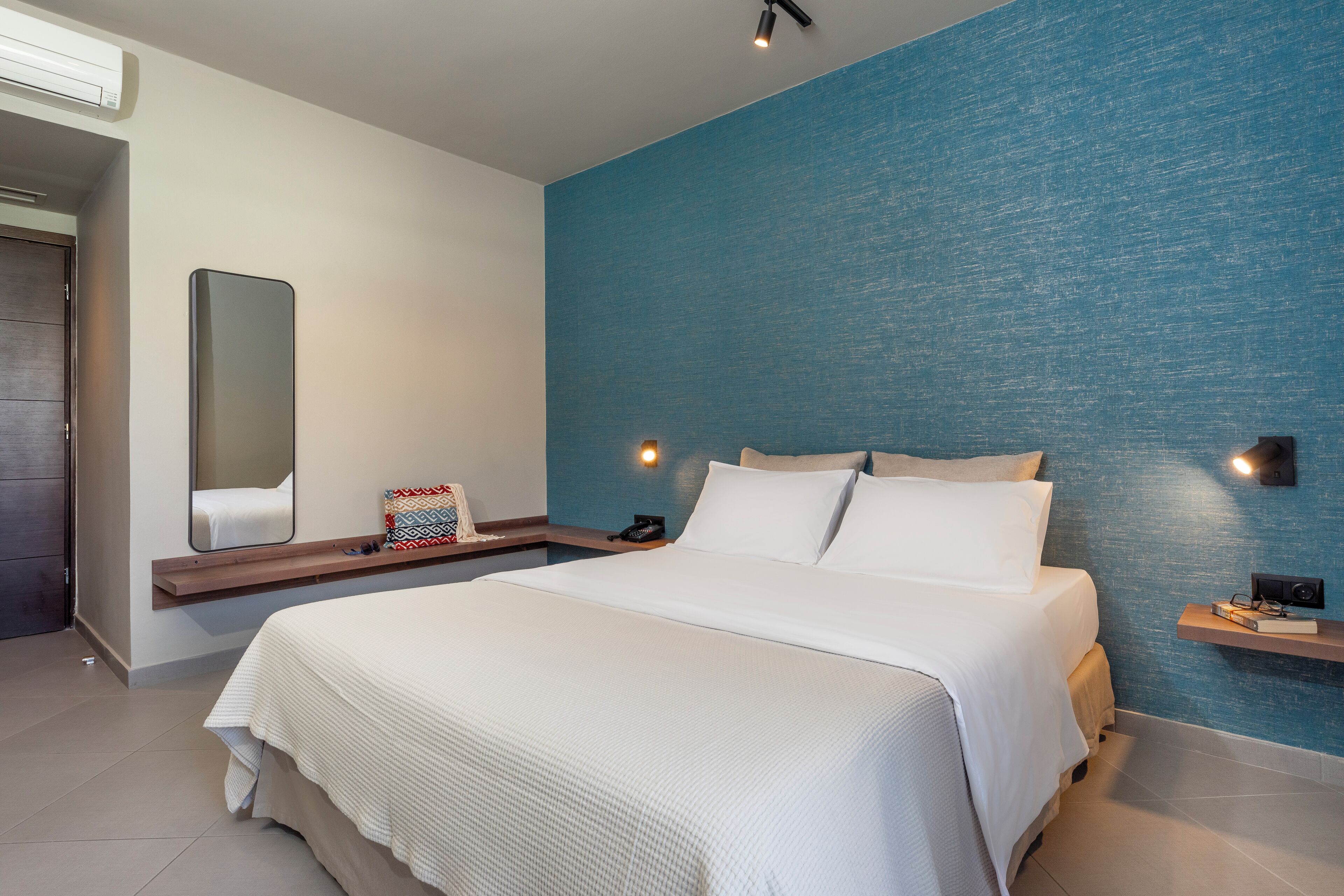 Ein modernes Hotelzimmer mit einem großen Bett, einem Nachttisch, einem Spiegel und einer blauen Akzentwand.
