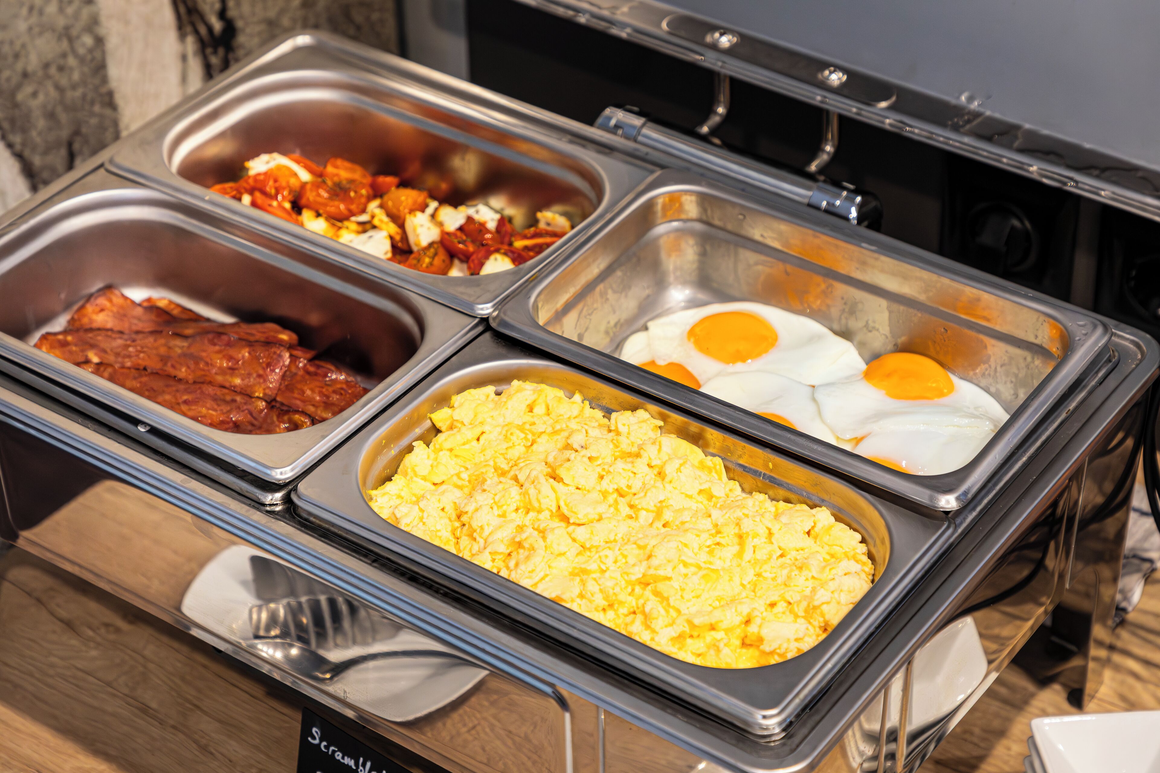 A buffet with various food options including scrambled eggs, bacon, and eggs benedict.