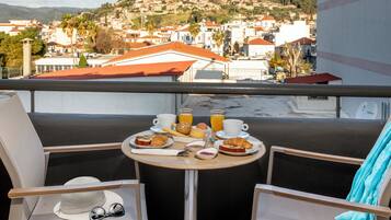 A balcony with a table set for breakfast, overlooking a hillside town.