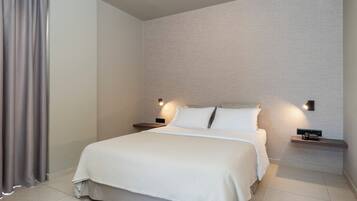 Una cama bien hecha con edredón blanco y almohadas, dos mesitas de noche con lámparas y una pared de color claro con textura.