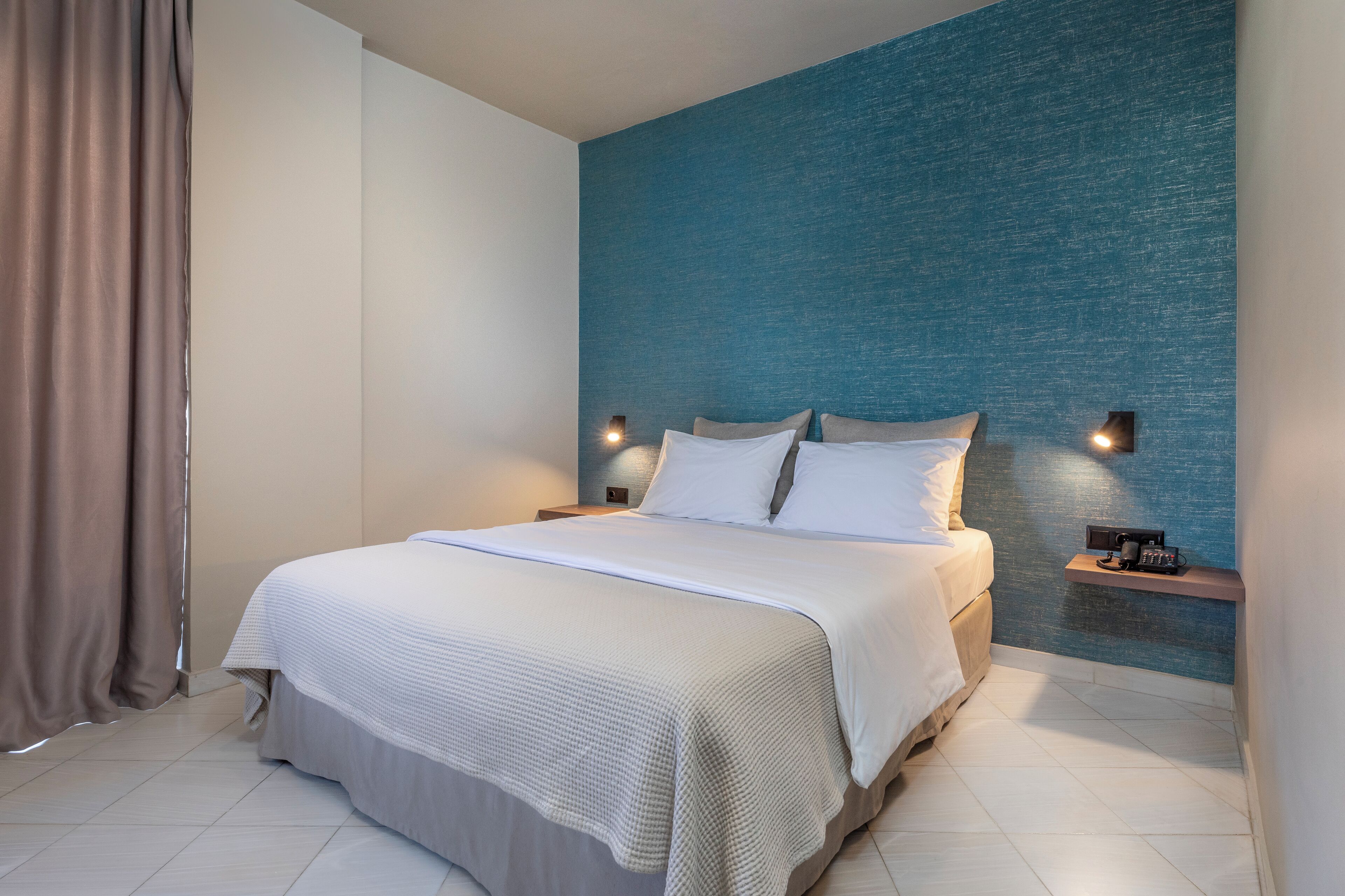 Moderni hotellihuone, jossa on suuri sänky, kaksi yöpöytää ja sininen tehosteseinä.