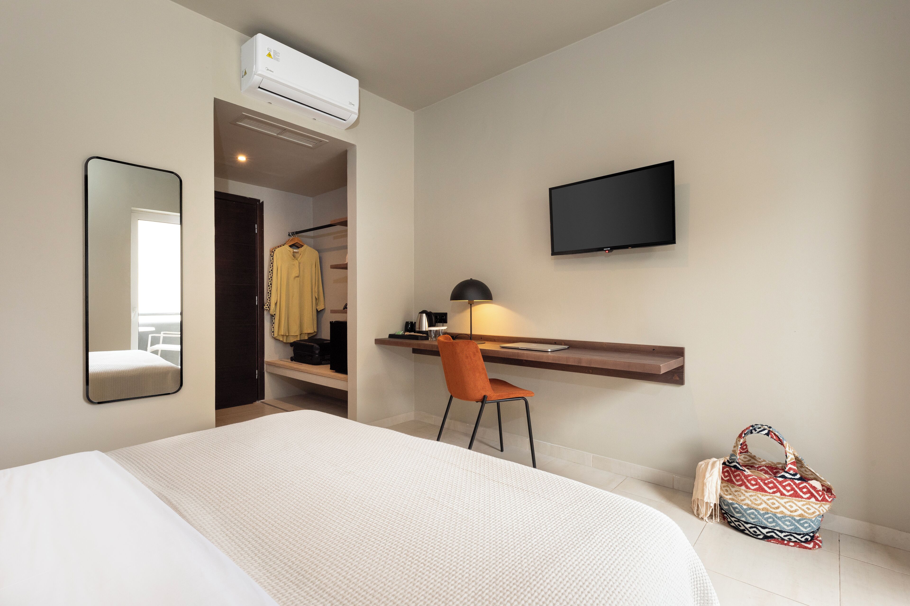 Habitación de hotel con cama, escritorio con silla, televisor y aire acondicionado.