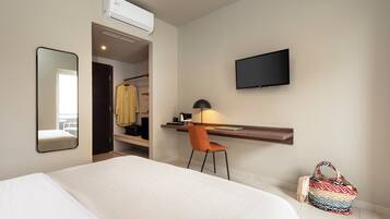 Habitación de hotel con cama, escritorio con silla, televisor y aire acondicionado.