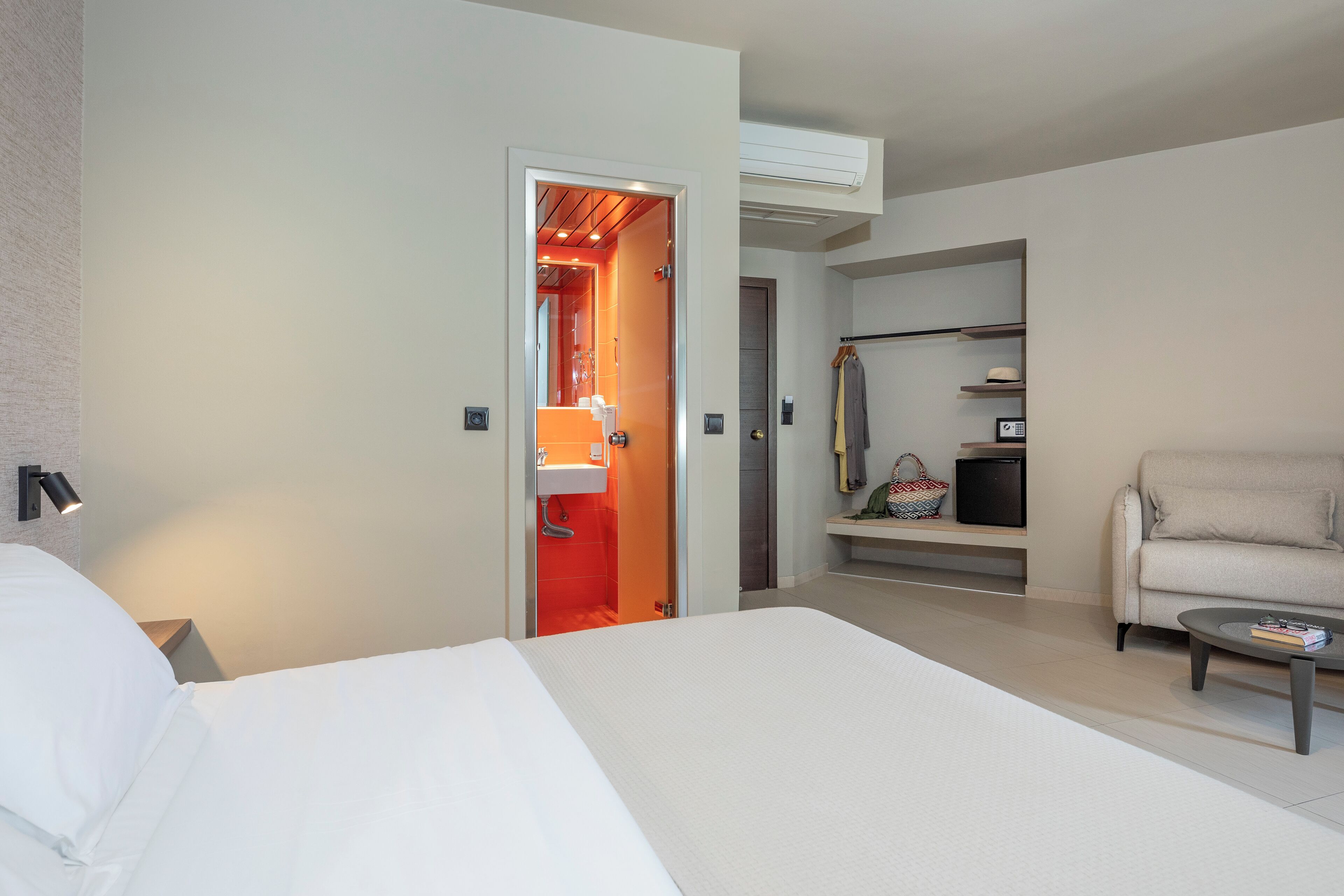 Habitación de hotel con cama, sofá, mesa de centro, armario y baño visible a través de una puerta abierta.