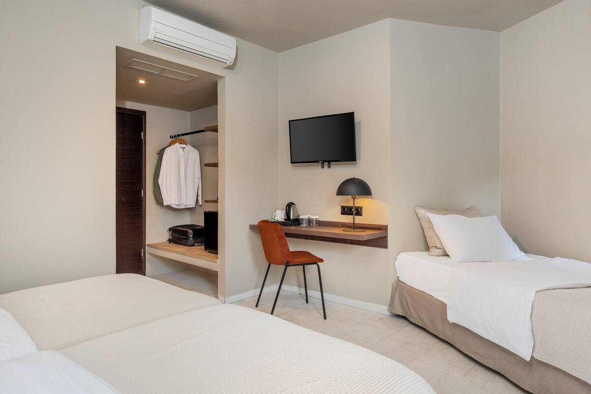 A hotel room with two beds, a desk with a chair, a TV mounted on the wall, and an air conditioning unit.