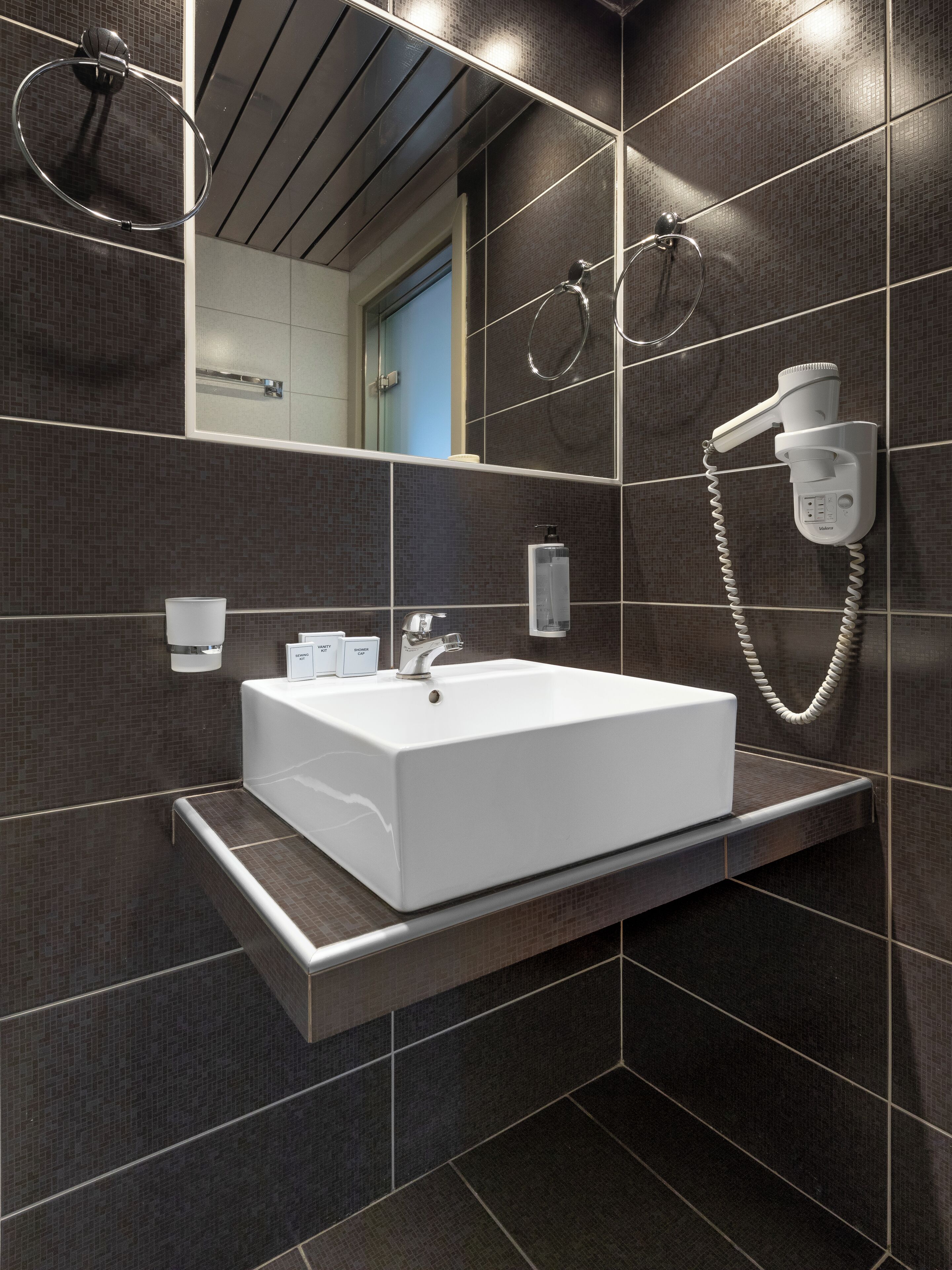 A modern bathroom with a large rectangular sink, a handheld showerhead, and a mirror reflecting a door.