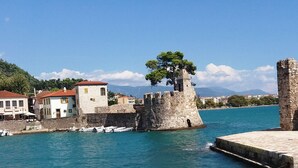 A coastal town with historic stone buildings, a prominent tower, and a statue on a fortified wall.