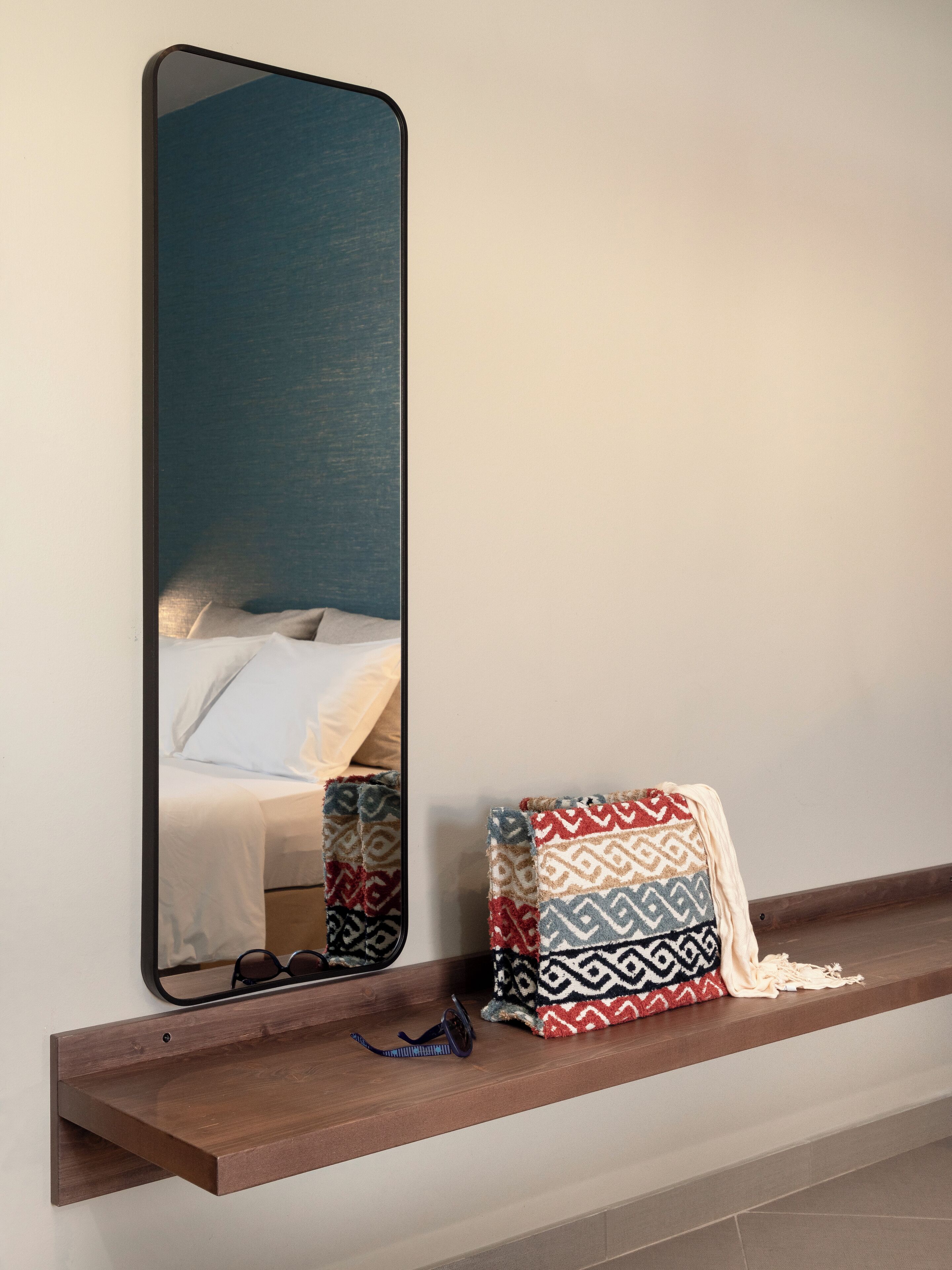 A mirror reflecting a bed with white linens and a patterned throw blanket on a shelf.