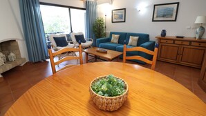 A living room with a wooden dining table, blue curtains, a blue sofa, and a fireplace. - 2 Bedroom Apartment with Swimming pool at São Rafael Beach - Albufeira (Albufeira)