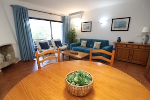 A living room with a wooden dining table, blue curtains, a blue sofa, and a fireplace. - 2 Bedroom Apartment with Swimming pool at São Rafael Beach - Albufeira (Albufeira)